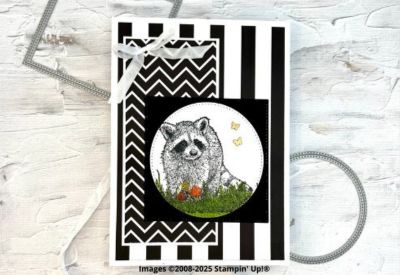 White card with a vertical black and white striped background mat with a black and white zigzag rectangle on the left side and a black square topped with a white circle with a black stamped image of a raccoon with green grass at its feet. There are also square and circle dies behind the card at the top left and bottom right.